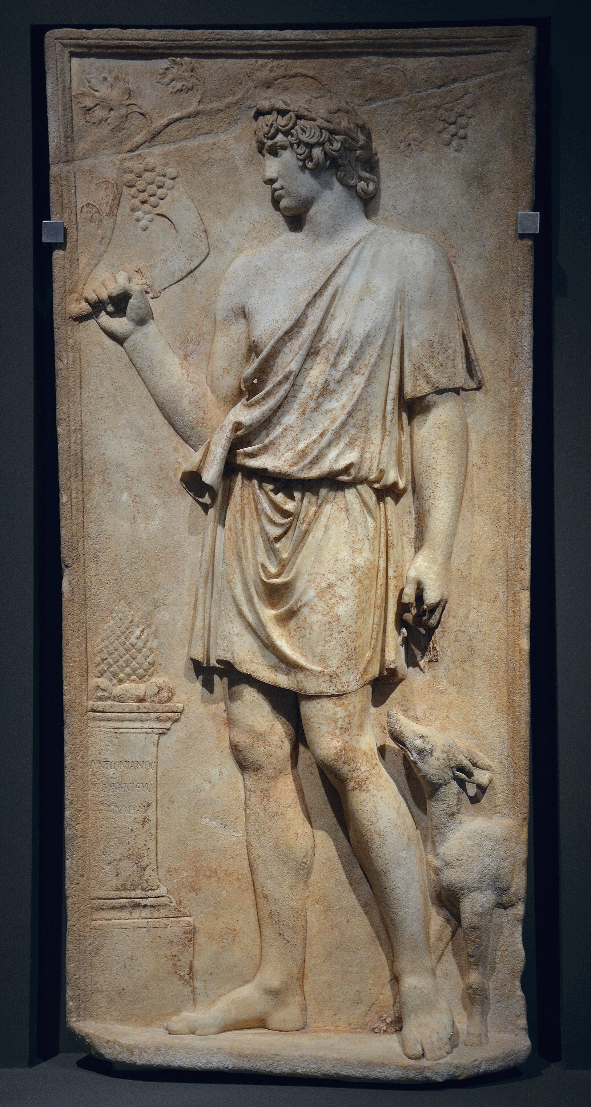 Antinous as Silvanus — marble relief of the woodland god with pruning hook, vine overhead, and his dog, 130–138 AD